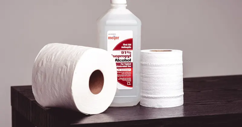 Bottle of isopropyl alcohol with tissue rolls on a wooden bench
