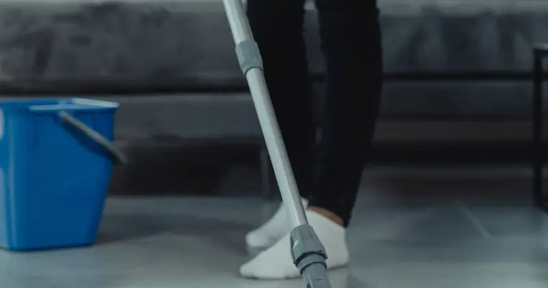 Person in gray sweater mopping and cleaning the floor