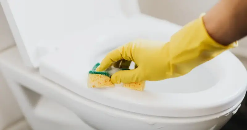 A cleaner in full protective gear disinfects a table indoors, ensuring a sterile environment.