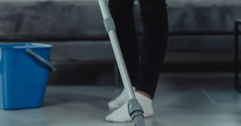 Person in gray sweater mopping and cleaning the floor